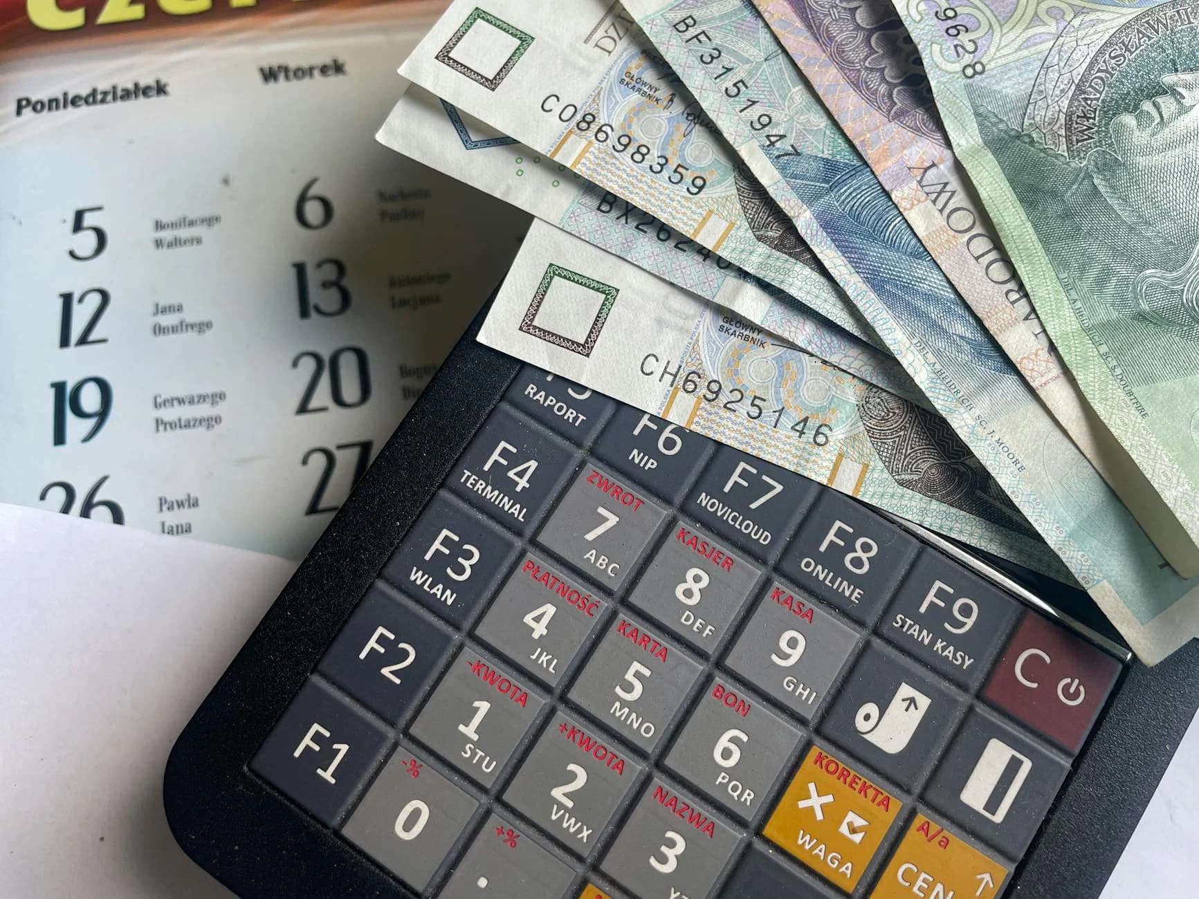 Nahaufnahme polnischer Zloty-Banknoten auf einem Taschenrechner mit einem Kalender im Hintergrund.