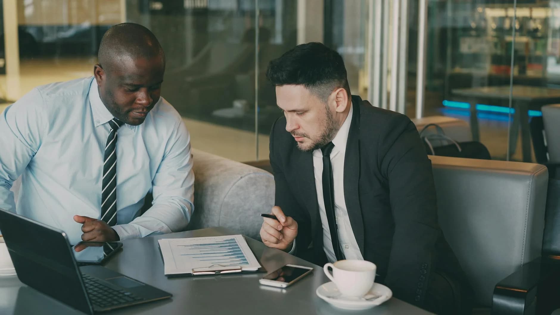 Zwei Geschäftsleute besprechen in ihrem Büro mit Laptop und Kaffee einen Finanzbericht.